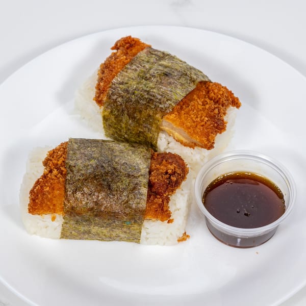 Two hibachi chicken katsu musubi with nori wraps and a side of sauce on a white plate.