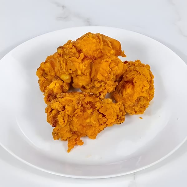 Three pieces of crispy, golden-brown fried chicken are presented on a white plate.