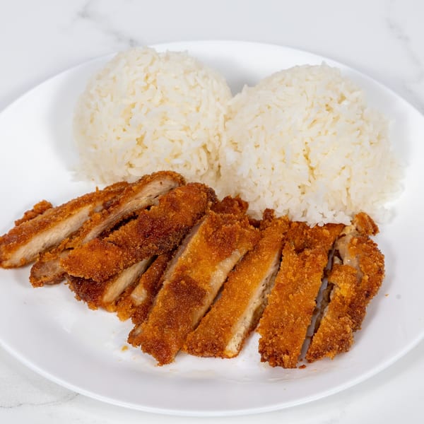 Crispy fried chicken cutlets, sliced and served with two mounds of white rice on a white plate.