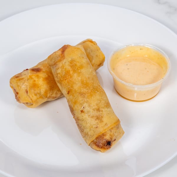 Two crispy hibachi egg rolls with a side of creamy dipping sauce on a white plate.