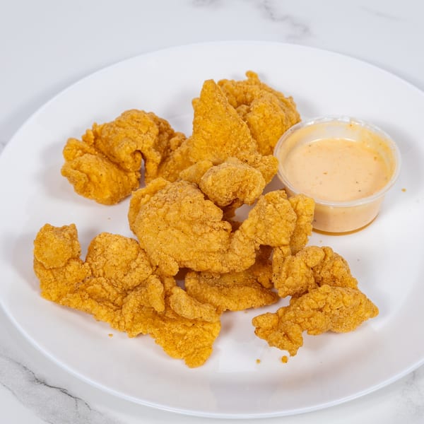 A white plate holds golden-brown fried chicken pieces and a small cup of dipping sauce.
